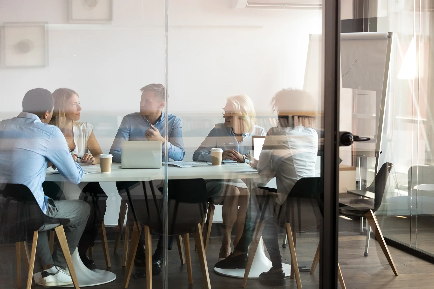 Business Team sitzt ins Gespräch vertieft im Besprechungsraum eines Büros, Blick von außen durch die Glasscheibe | Erika Götz, Teamcoaching
